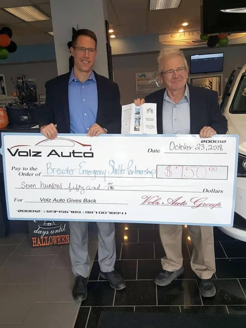 Two men are standing with banner cheque inside a nice showroom.
