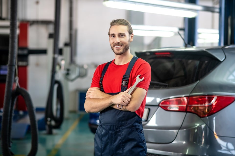 Smiling auto mechanic holding a wrench while standing in a car service garage.